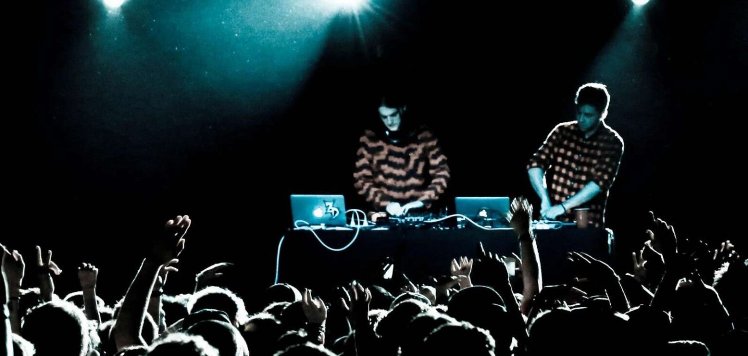 Дуэт Zeds Dead за пультом на сцене, перед ними тёмный зал с поднятыми руками