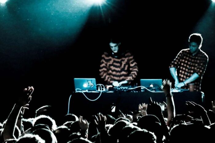 Дуэт Zeds Dead за пультом на сцене, перед ними тёмный зал с поднятыми руками